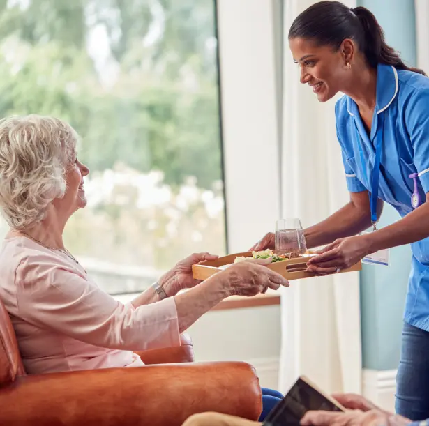 A nurse handing food to an elderly woman.