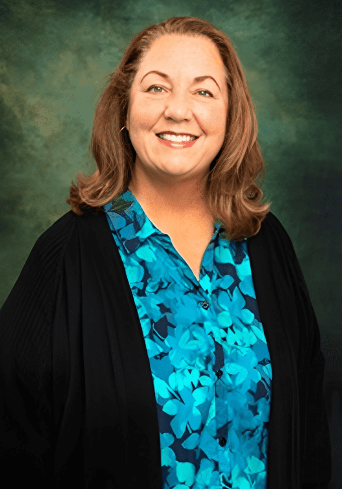 A woman in black jacket and blue shirt smiling.