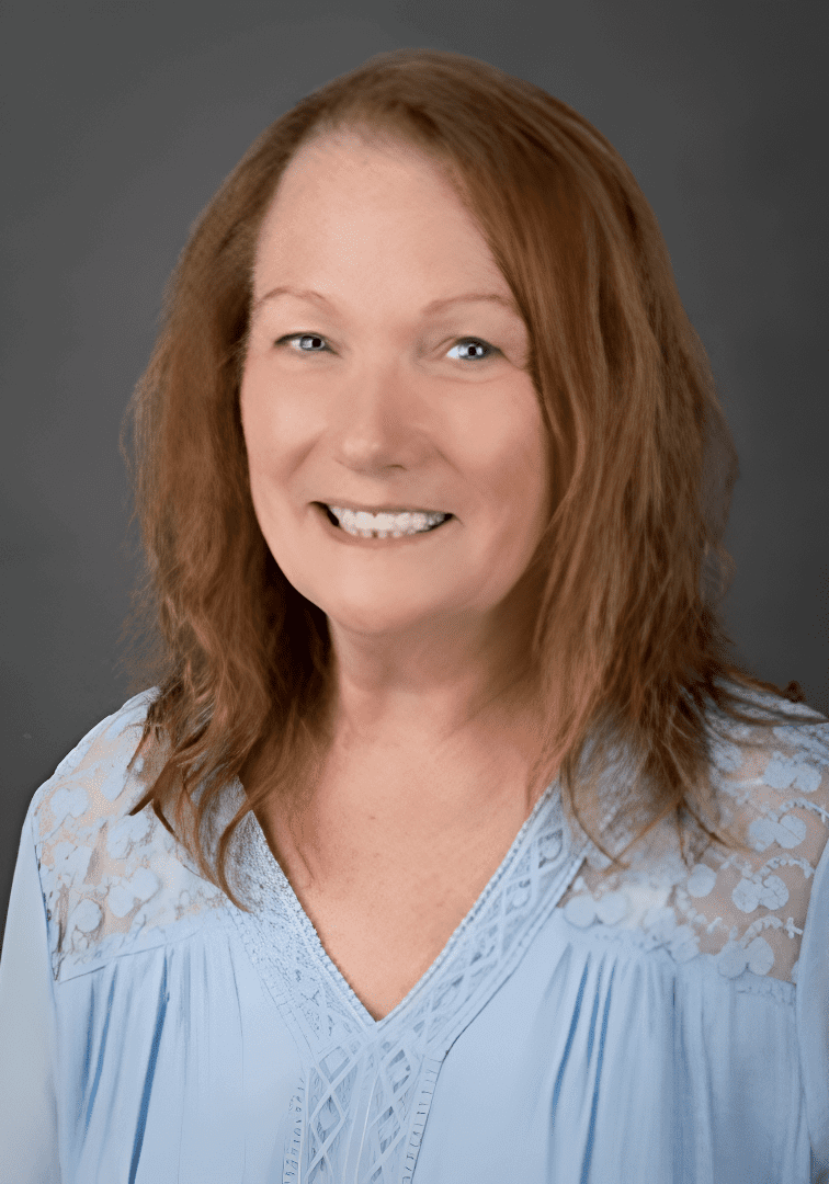 A woman with red hair and blue shirt smiling.
